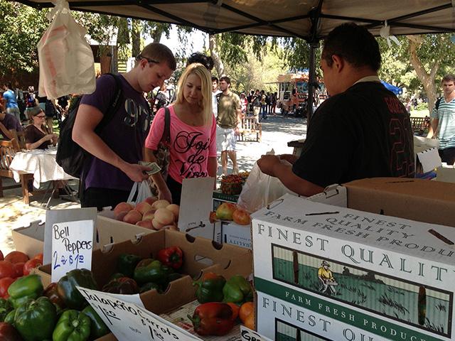 a male and female student buying produce from a vendor at the farmer's market on campus
