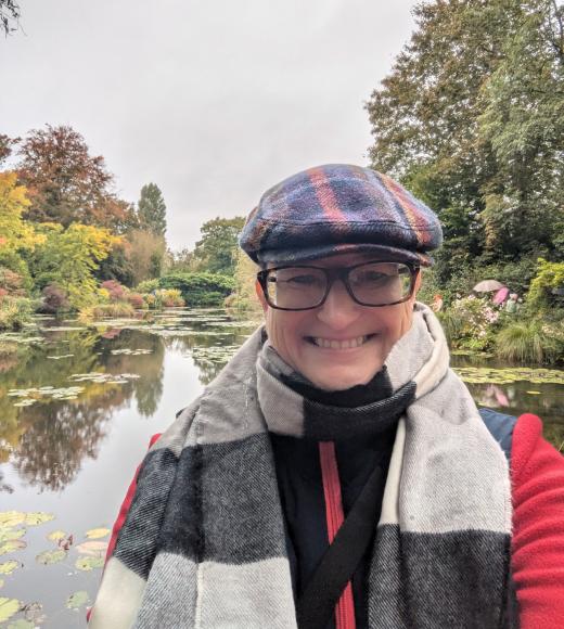 Picture of a smiling person wearing a grey cap, glasses, and a striped scarf